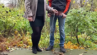 Hot milf in pantyhose and skirt holding guy's cock outdoors while pissing